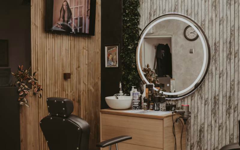 Barber suite with black barber chair, wood vanity and round lit mirror