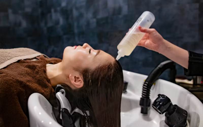 Client enjoying a relaxing head spa scalp treatment at a shampoo bowl in Prosper TX